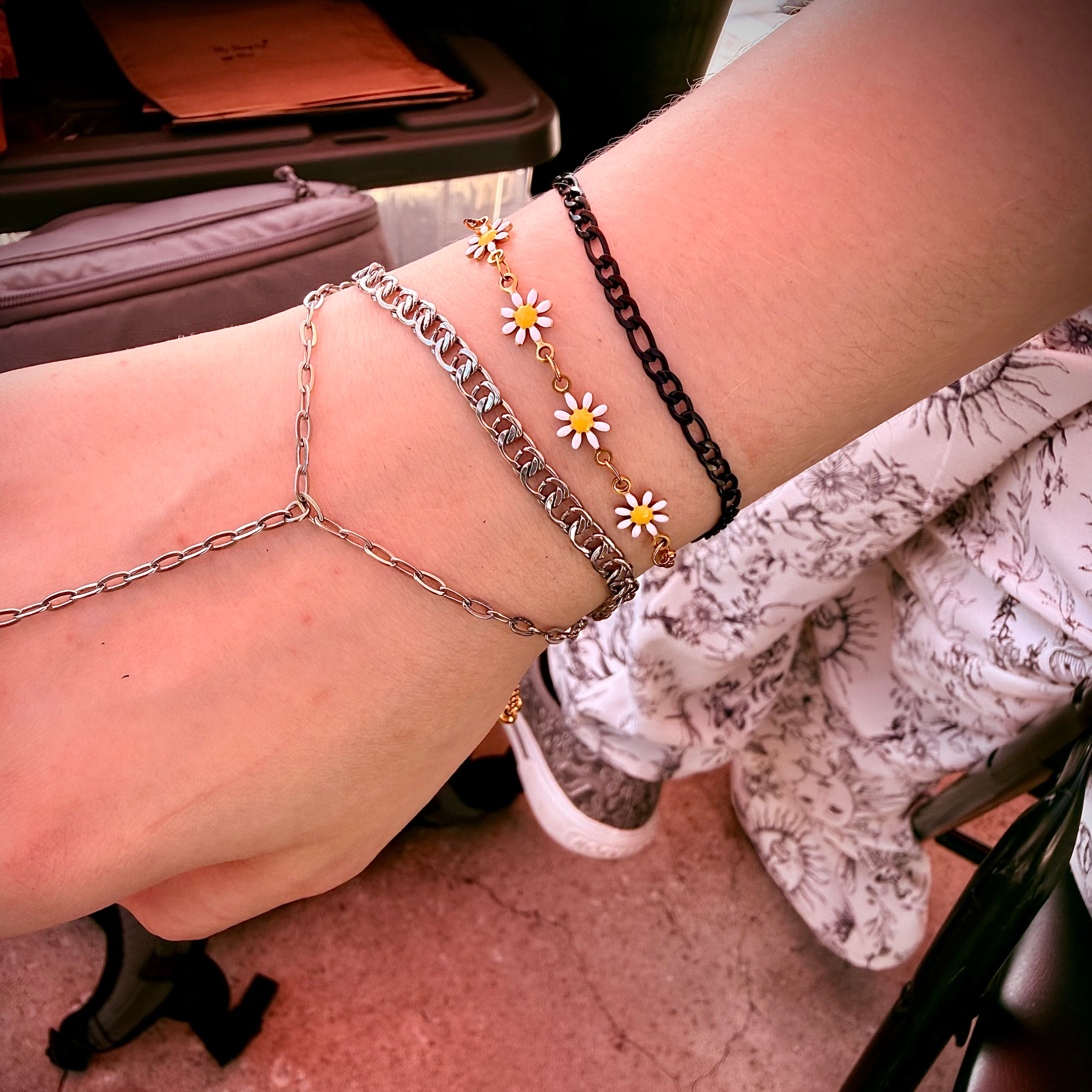 Daisy charm and layered permanent bracelets worn on Skylar's wrist